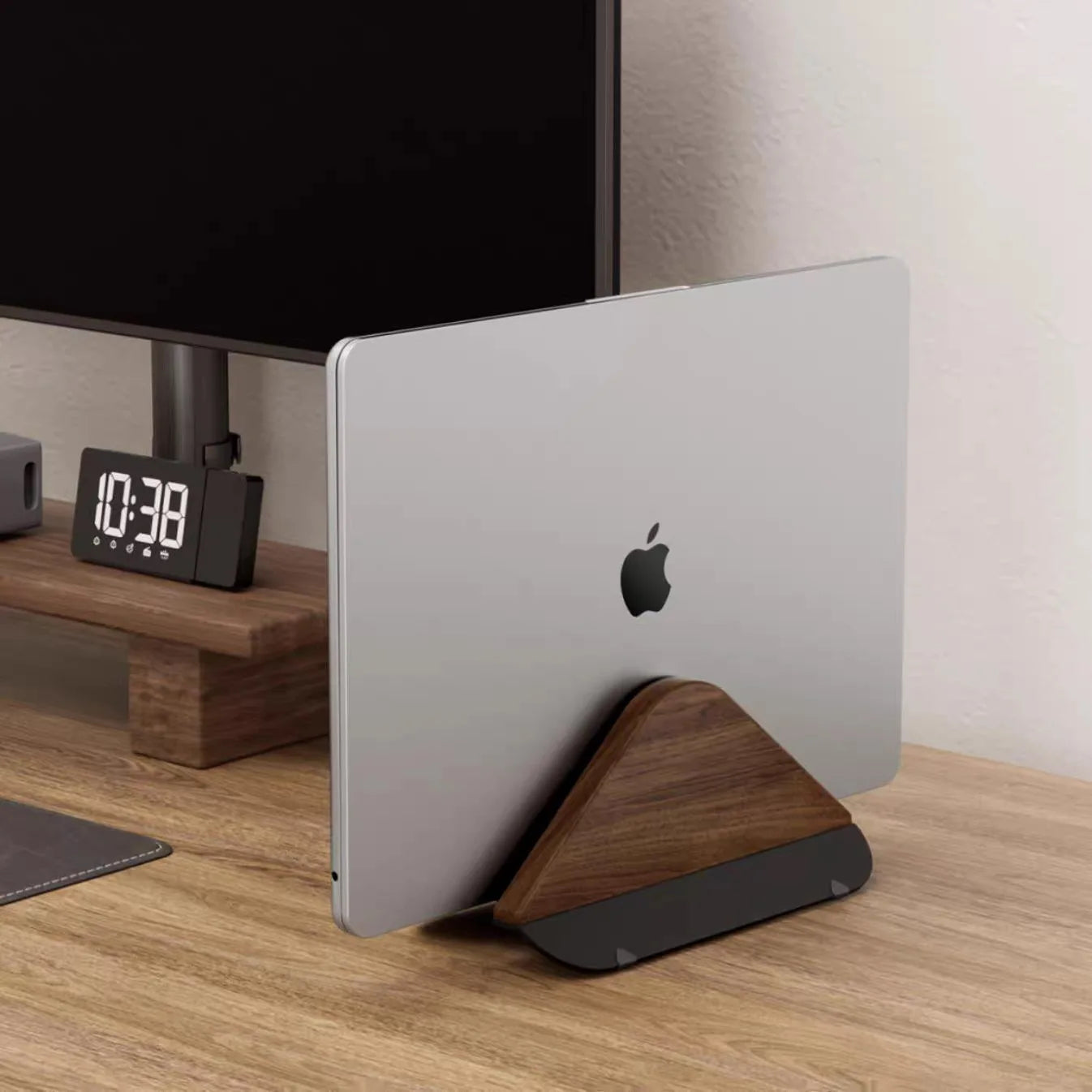 Laptop on a wooden stand with an Apple logo on a desk next to a digital clock.