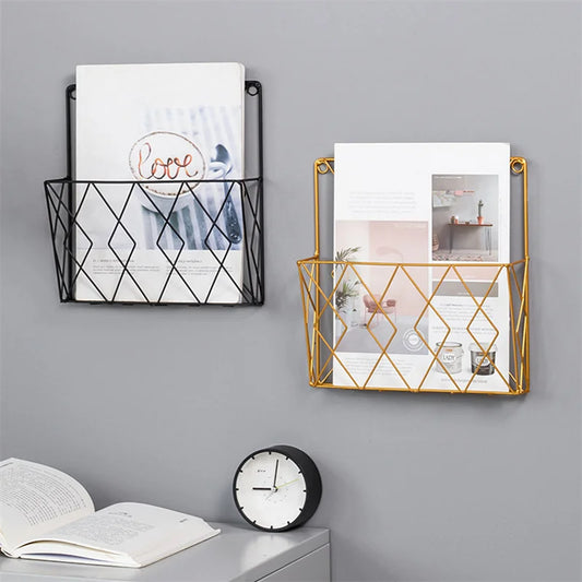 Two wall-mounted metal magazine holders with books on a gray wall, below an open book and clock.